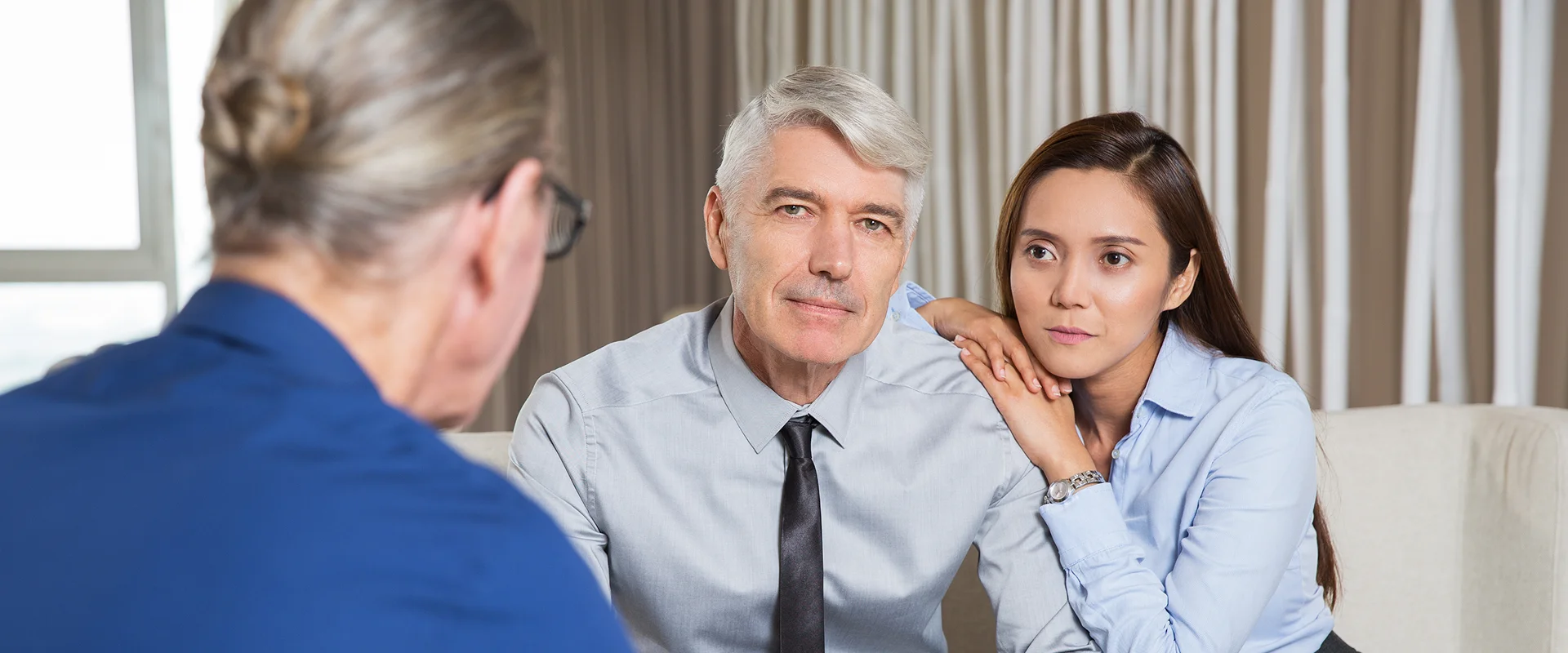 A senior man and a young woman sitting on a sofa and listening intently during a meeting.